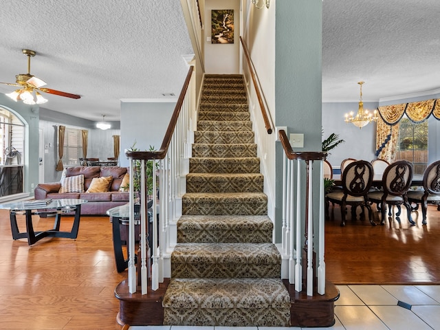 stairs featuring hardwood / wood-style floors, ceiling fan with notable chandelier, crown molding, and a textured ceiling