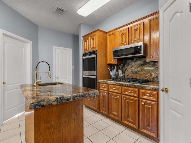 kitchen featuring appliances with stainless steel finishes, a textured ceiling, a kitchen island with sink, sink, and light tile patterned flooring