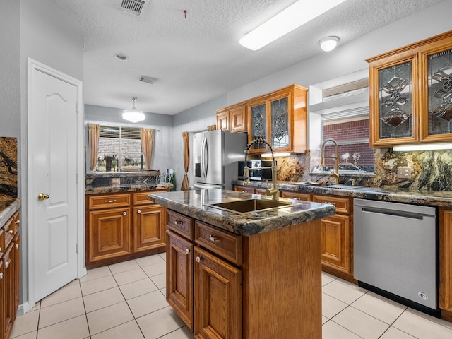 kitchen featuring decorative backsplash, a textured ceiling, stainless steel appliances, and a kitchen island with sink