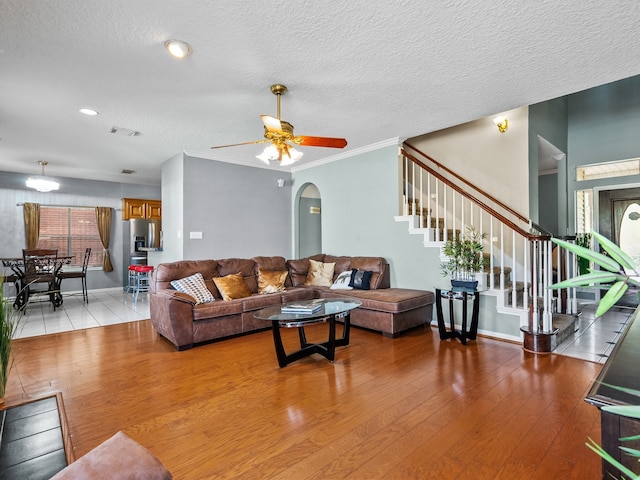 living room with a textured ceiling, light wood-type flooring, ceiling fan, and ornamental molding