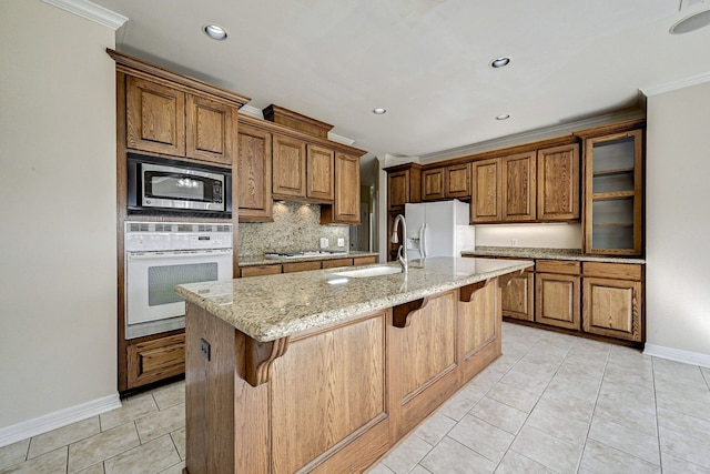 kitchen with light stone counters, a kitchen island with sink, stainless steel appliances, a breakfast bar area, and light tile patterned floors