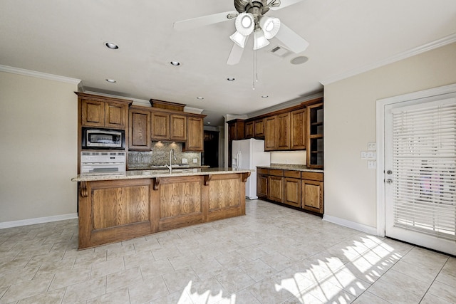 kitchen with ceiling fan, decorative backsplash, a kitchen island with sink, white appliances, and a kitchen breakfast bar