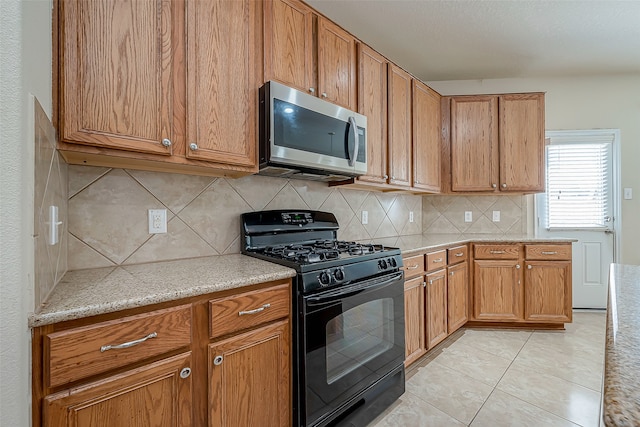 kitchen with backsplash, black gas stove, light tile patterned floors, and light stone counters