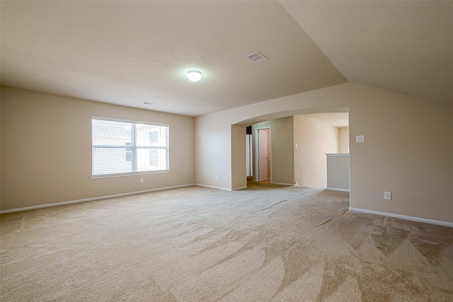 empty room with a textured ceiling, light carpet, and vaulted ceiling