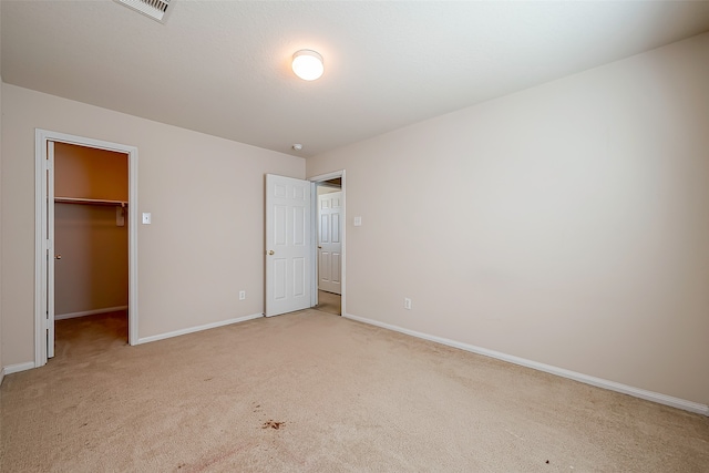 unfurnished bedroom with a walk in closet, light carpet, and a closet