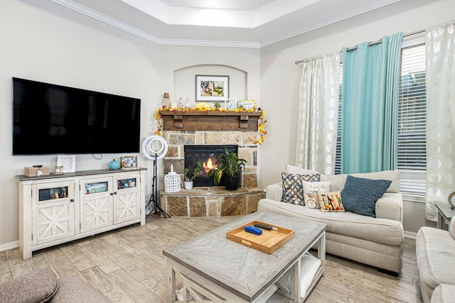 living room with light wood-type flooring, a fireplace, crown molding, and a tray ceiling