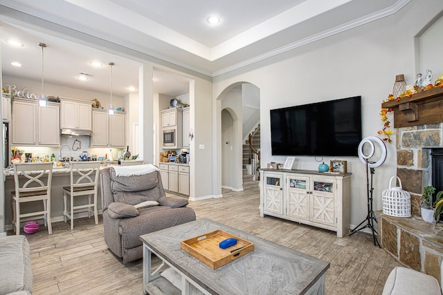 living room featuring a fireplace, light hardwood / wood-style flooring, crown molding, and a tray ceiling