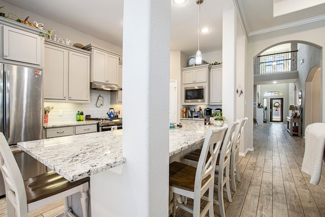 kitchen featuring stainless steel appliances, light stone countertops, hanging light fixtures, light hardwood / wood-style floors, and a kitchen breakfast bar