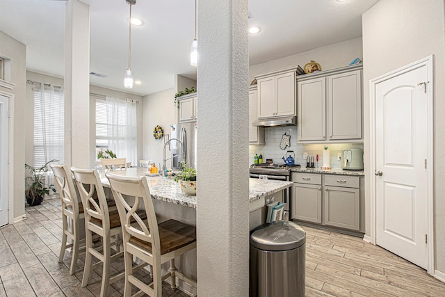 kitchen featuring appliances with stainless steel finishes, light stone countertops, decorative light fixtures, light hardwood / wood-style flooring, and gray cabinets