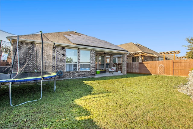 rear view of house featuring solar panels, a patio area, a lawn, and a trampoline