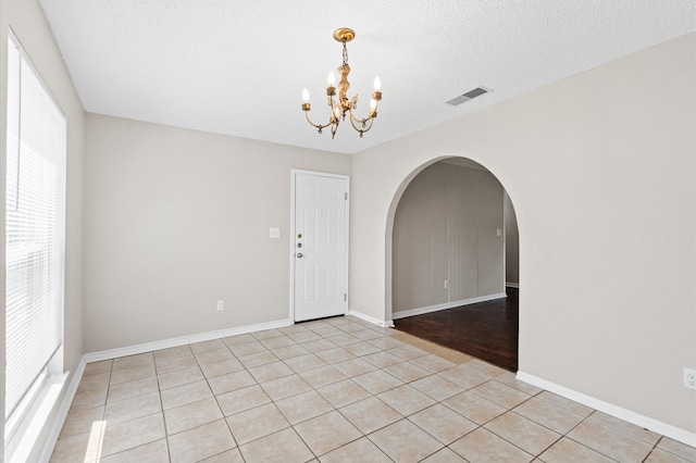 empty room featuring light wood-type flooring, plenty of natural light, a chandelier, and a textured ceiling