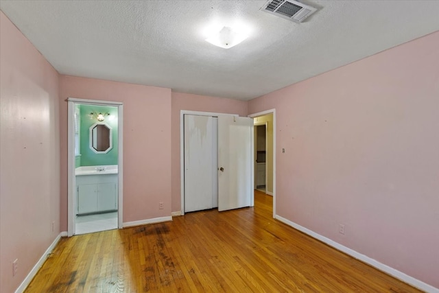 unfurnished bedroom featuring connected bathroom, a closet, light hardwood / wood-style floors, and a textured ceiling