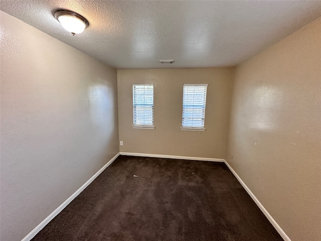 unfurnished room with dark carpet and a textured ceiling