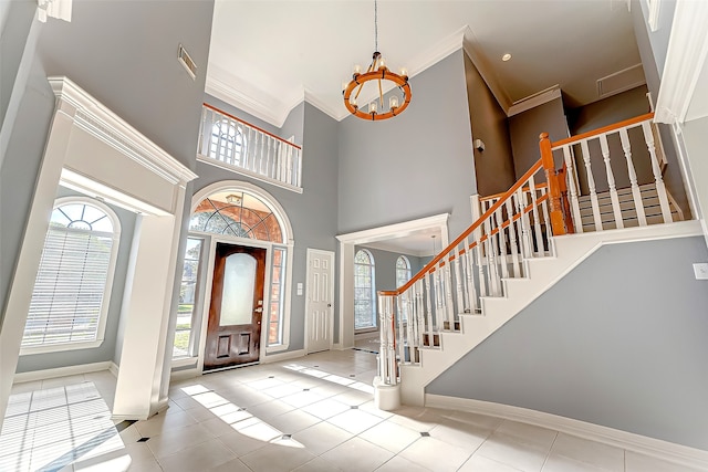 tiled foyer entrance with ornamental molding, a towering ceiling, a wealth of natural light, and an inviting chandelier