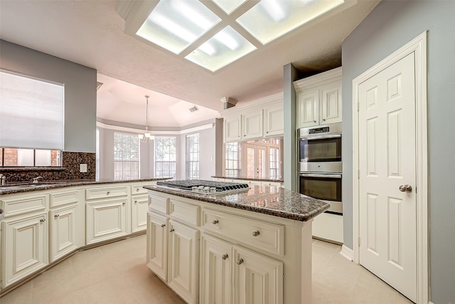 kitchen with stainless steel appliances, a kitchen island, hanging light fixtures, decorative backsplash, and dark stone countertops