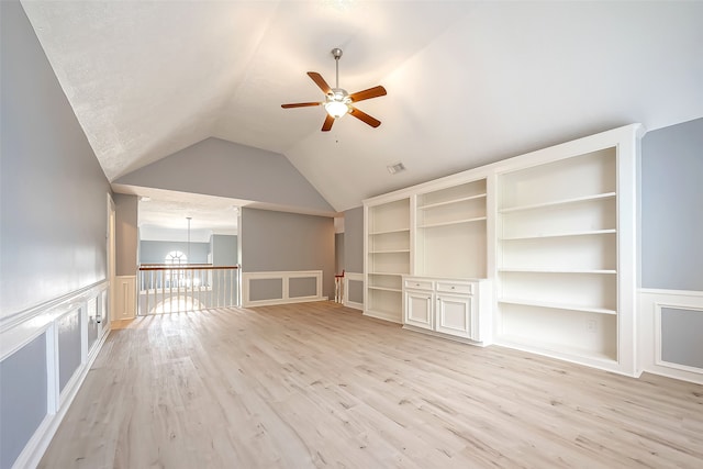 unfurnished living room with built in features, ceiling fan with notable chandelier, light hardwood / wood-style flooring, and vaulted ceiling