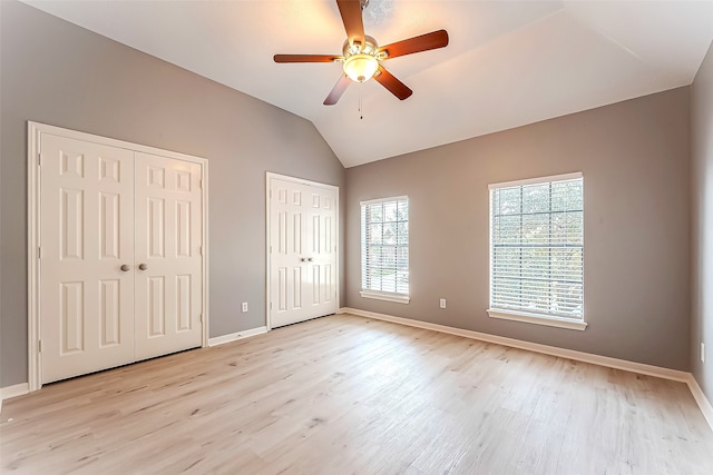 unfurnished bedroom featuring light hardwood / wood-style floors, lofted ceiling, ceiling fan, and two closets