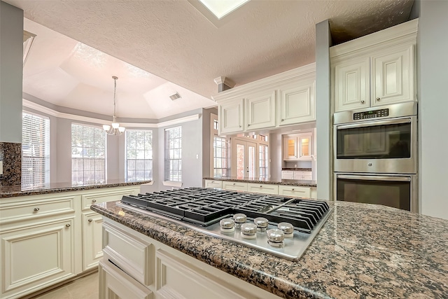 kitchen featuring dark stone countertops, appliances with stainless steel finishes, vaulted ceiling, and cream cabinetry