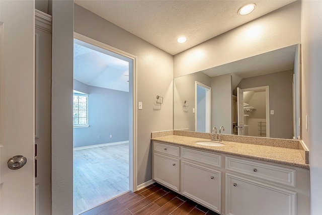 bathroom with vanity, hardwood / wood-style floors, vaulted ceiling, and a textured ceiling