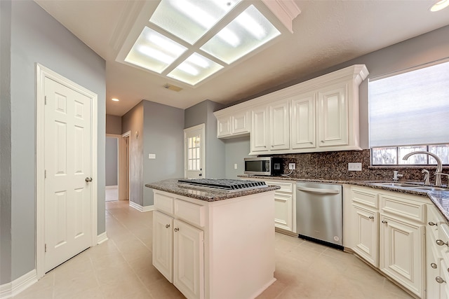 kitchen with stainless steel appliances, sink, dark stone counters, a kitchen island, and decorative backsplash