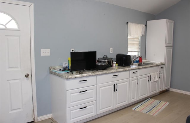 kitchen featuring white cabinets, light stone countertops, light wood-type flooring, and sink