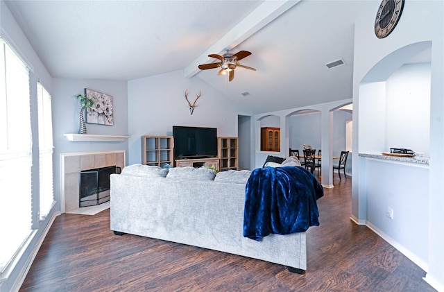 living room with ceiling fan, lofted ceiling with beams, dark wood-type flooring, and a tiled fireplace