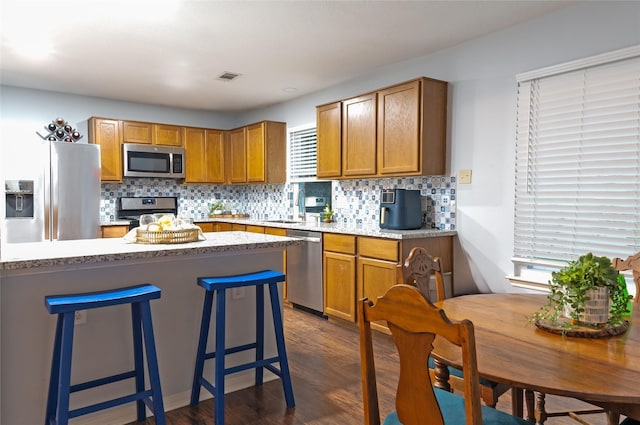 kitchen featuring a kitchen breakfast bar, dark hardwood / wood-style flooring, tasteful backsplash, stainless steel appliances, and sink