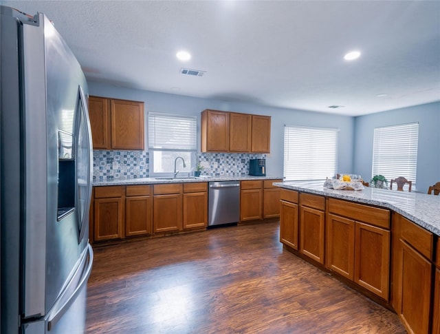 kitchen featuring sink, dark wood-type flooring, stainless steel appliances, tasteful backsplash, and light stone counters