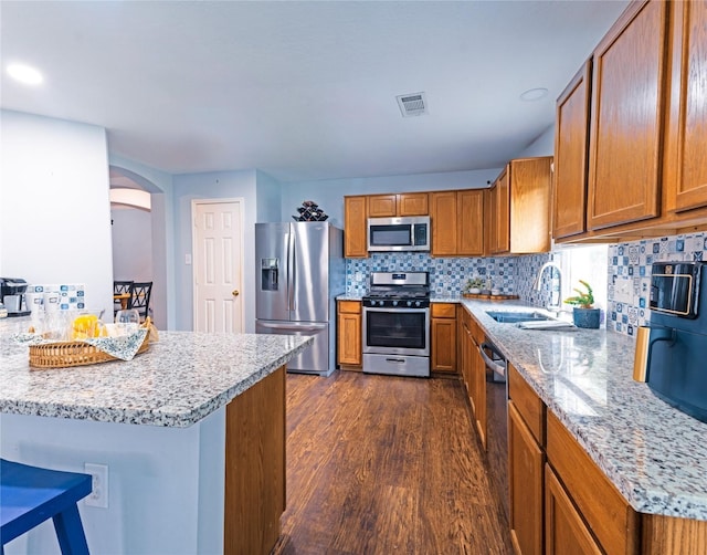 kitchen with sink, dark hardwood / wood-style floors, appliances with stainless steel finishes, light stone counters, and a breakfast bar area