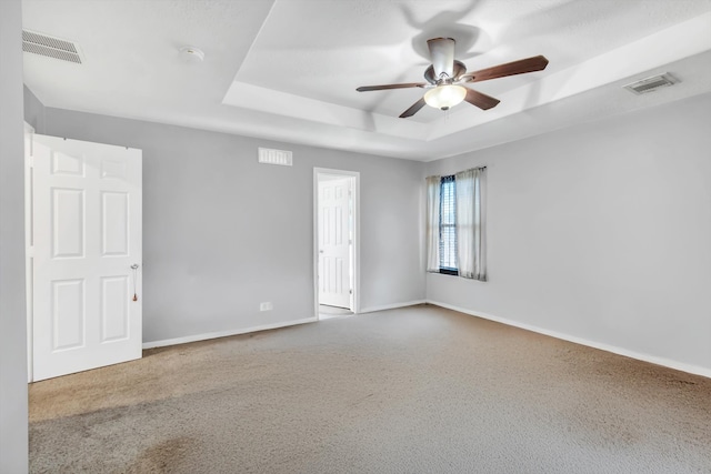 carpeted spare room featuring ceiling fan and a raised ceiling