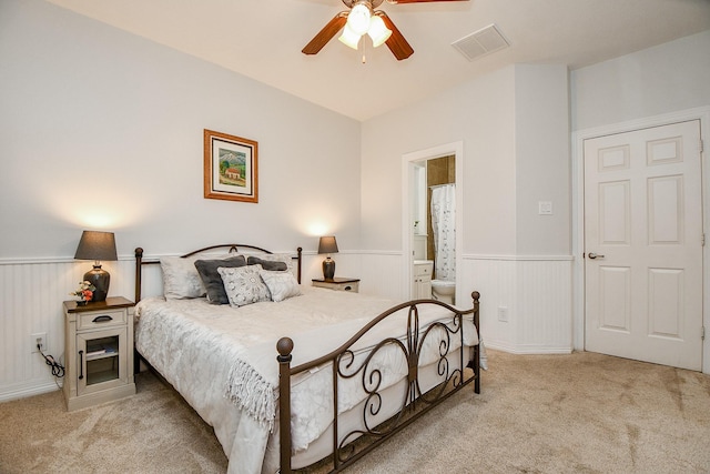 carpeted bedroom with visible vents, ceiling fan, connected bathroom, and wainscoting