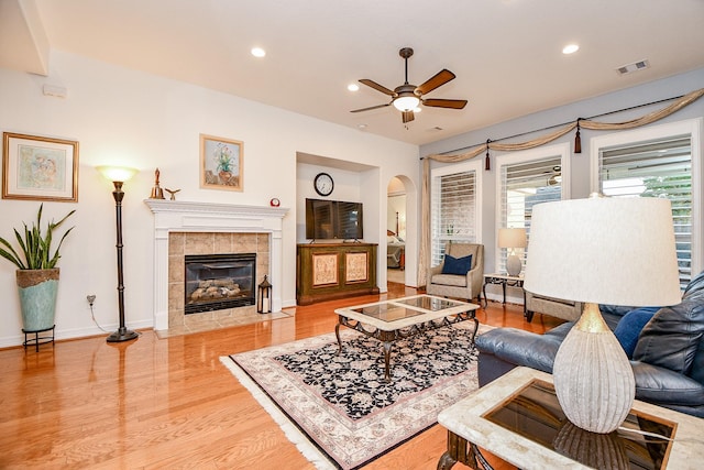 living room with ceiling fan, wood-type flooring, and a tile fireplace