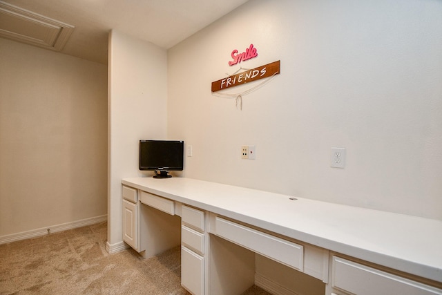 unfurnished office with baseboards, built in desk, and light colored carpet