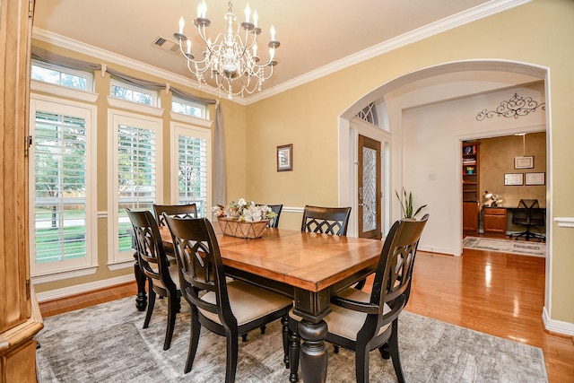 dining space featuring hardwood / wood-style floors, an inviting chandelier, a healthy amount of sunlight, and ornamental molding