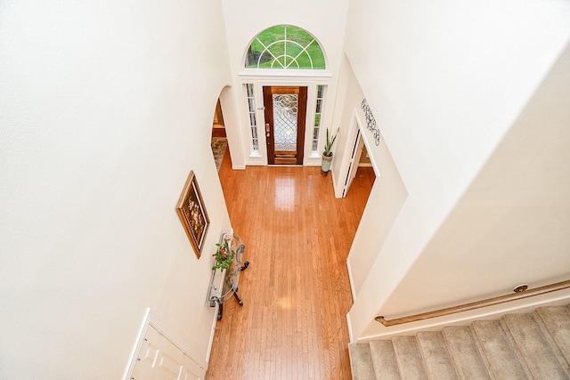 entryway with stairway, light wood-type flooring, arched walkways, and a towering ceiling