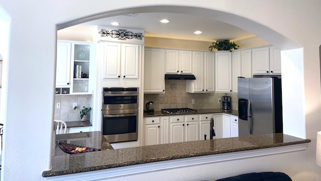 kitchen with white cabinetry, under cabinet range hood, arched walkways, and stainless steel appliances