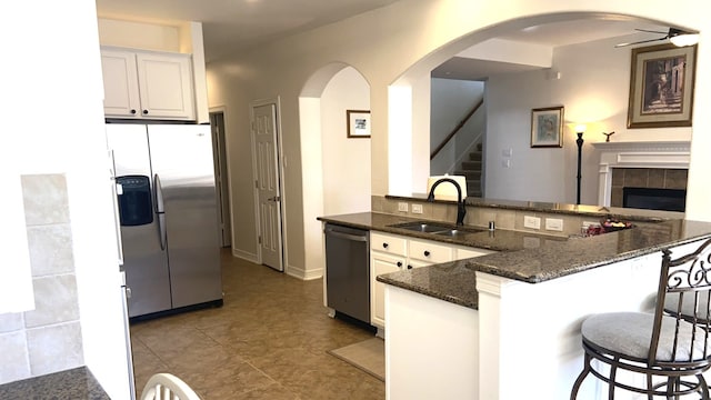 kitchen featuring dark stone countertops, ceiling fan, stainless steel appliances, arched walkways, and a sink