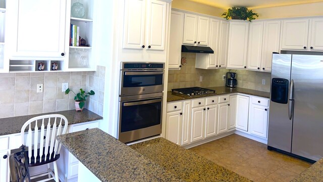 kitchen featuring backsplash, white cabinets, dark stone countertops, appliances with stainless steel finishes, and light tile patterned flooring