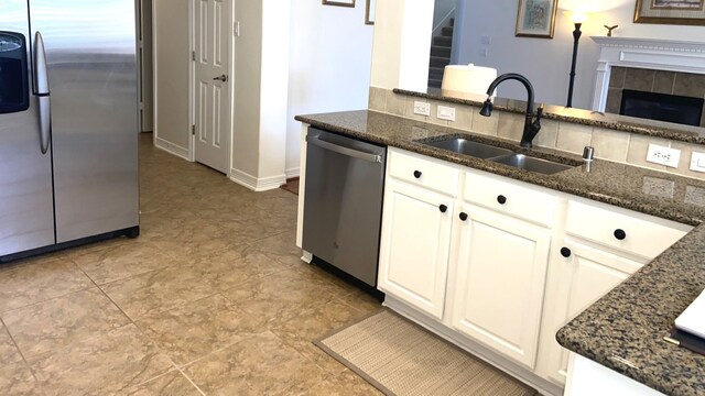 kitchen featuring appliances with stainless steel finishes, sink, a tile fireplace, dark stone countertops, and white cabinets