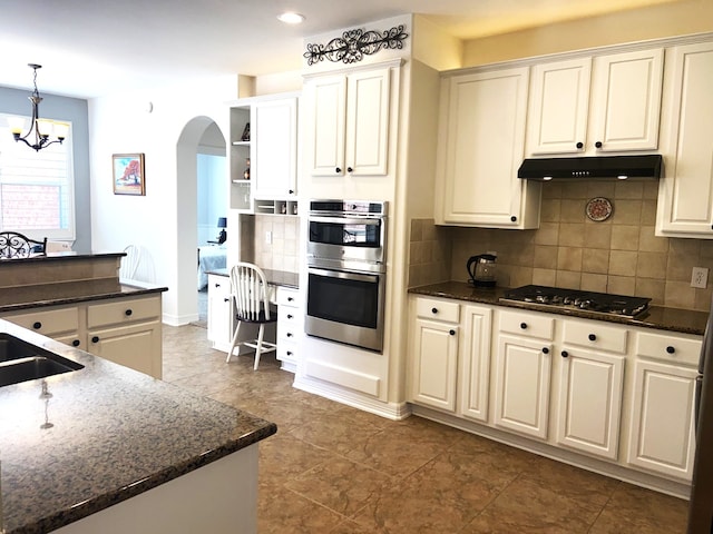 kitchen featuring stainless steel appliances, arched walkways, backsplash, open shelves, and under cabinet range hood