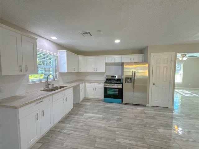 kitchen featuring sink, light stone counters, stainless steel appliances, white cabinets, and a textured ceiling