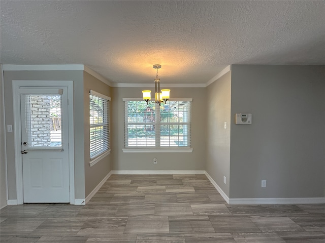 unfurnished dining area featuring crown molding, an inviting chandelier, a textured ceiling, and a healthy amount of sunlight