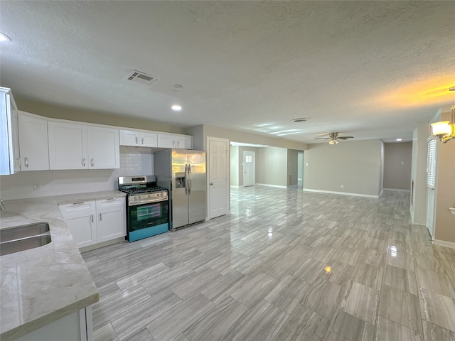 kitchen with ceiling fan with notable chandelier, sink, stainless steel appliances, light stone countertops, and white cabinetry