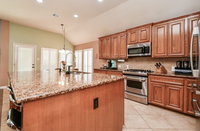 kitchen with sink, light stone counters, lofted ceiling, an island with sink, and appliances with stainless steel finishes