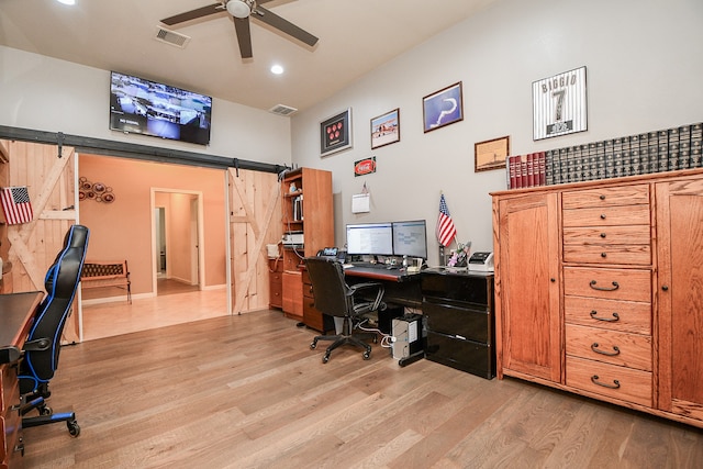 office area with a barn door, light hardwood / wood-style floors, and ceiling fan