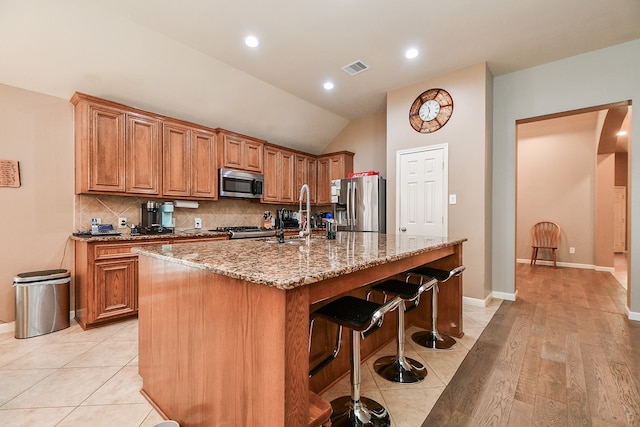 kitchen with light stone counters, sink, a kitchen island with sink, appliances with stainless steel finishes, and vaulted ceiling