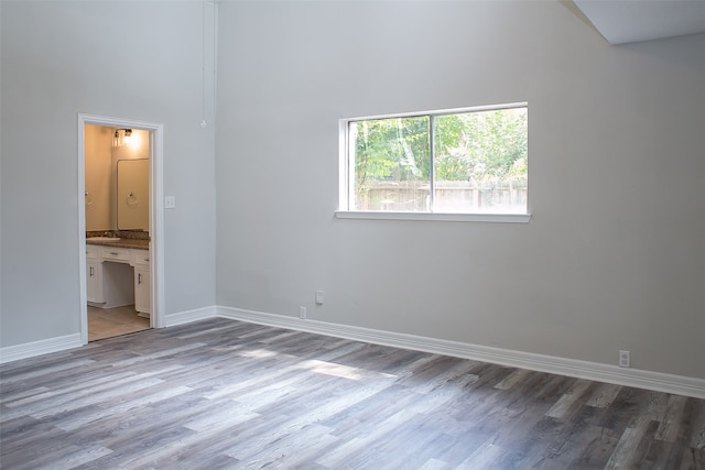 unfurnished bedroom featuring a towering ceiling, hardwood / wood-style floors, and ensuite bath