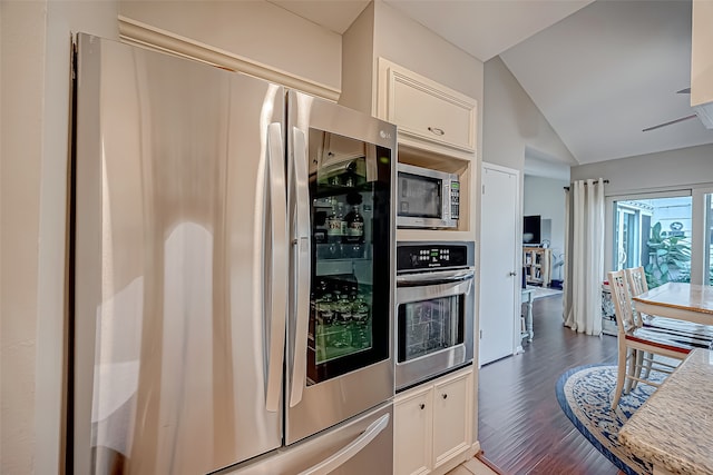 kitchen featuring dark wood-type flooring, white cabinets, stainless steel appliances, and vaulted ceiling