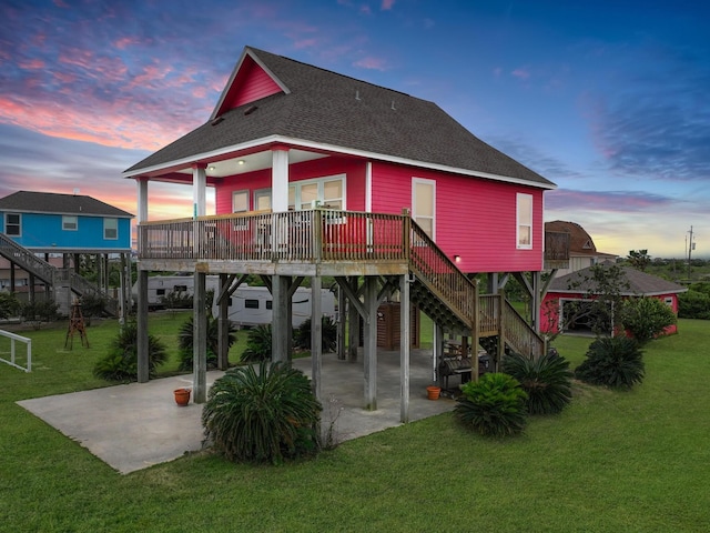 back house at dusk with a patio, a lawn, and a carport