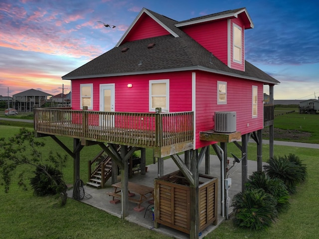 back house at dusk featuring a yard, a deck, a patio, and central AC unit